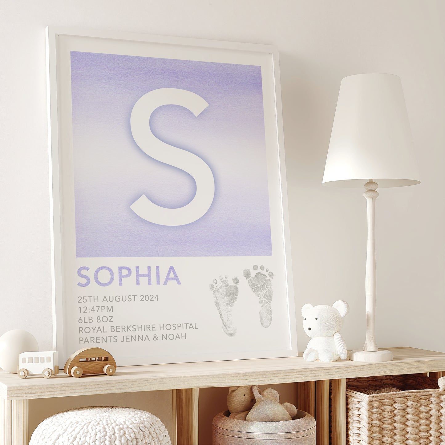 Framed print with a letter 'S', name 'Sophia', and birth details on a purple background, in a room with a lamp and toys.