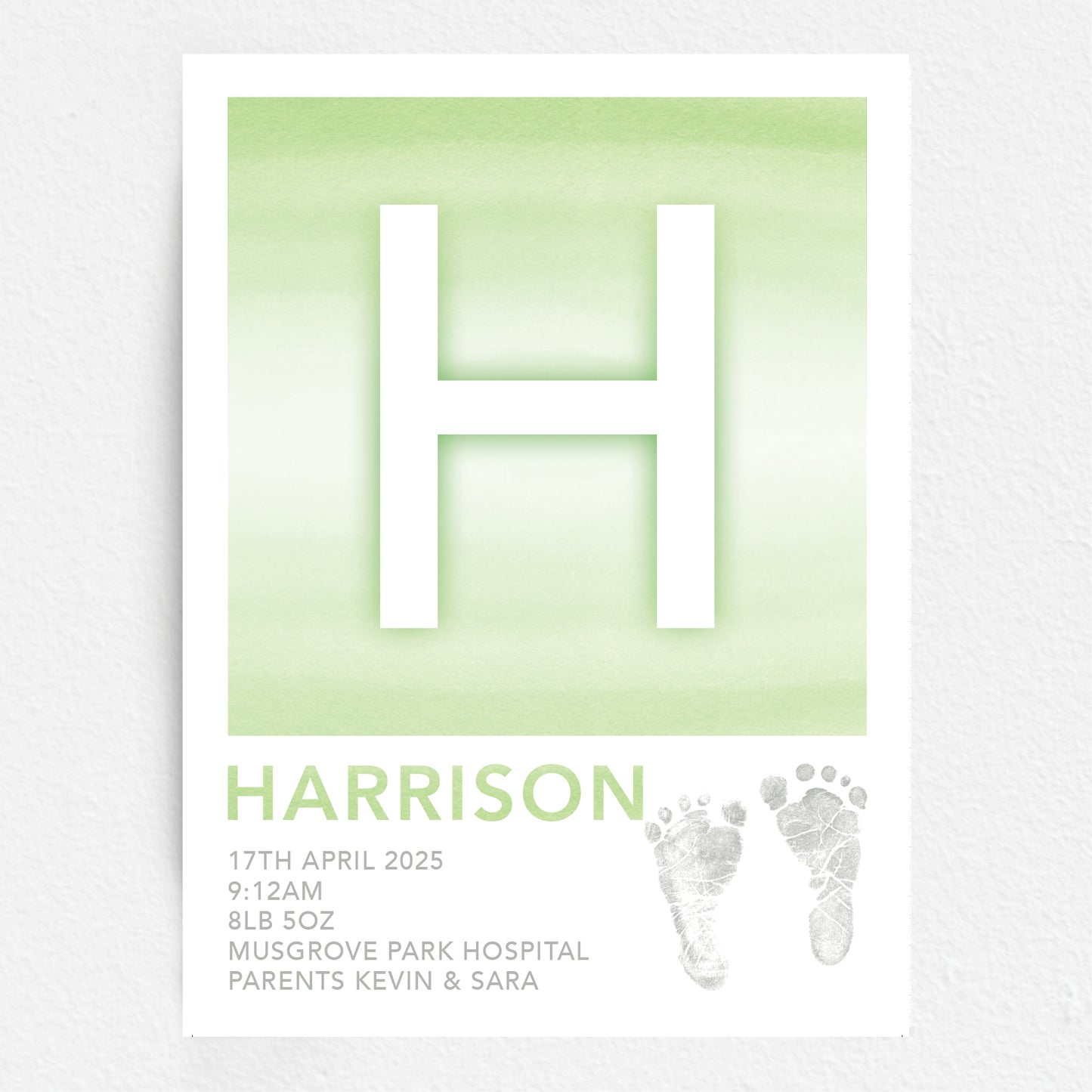 A personalised baby print with the initial 'H' in large green lettering, birth details, and baby feet prints.
