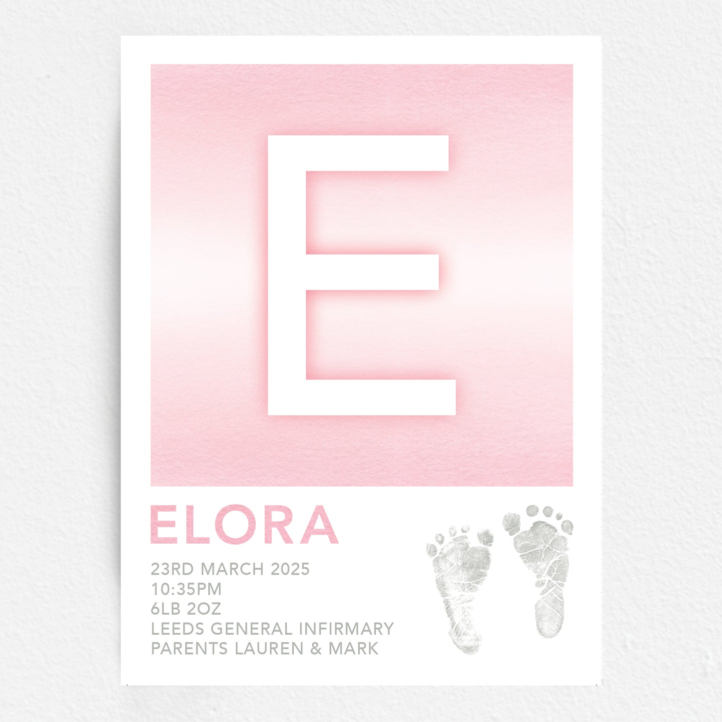 A personalised baby print with the initial 'E' in large pink lettering, birth details, and baby feet prints.