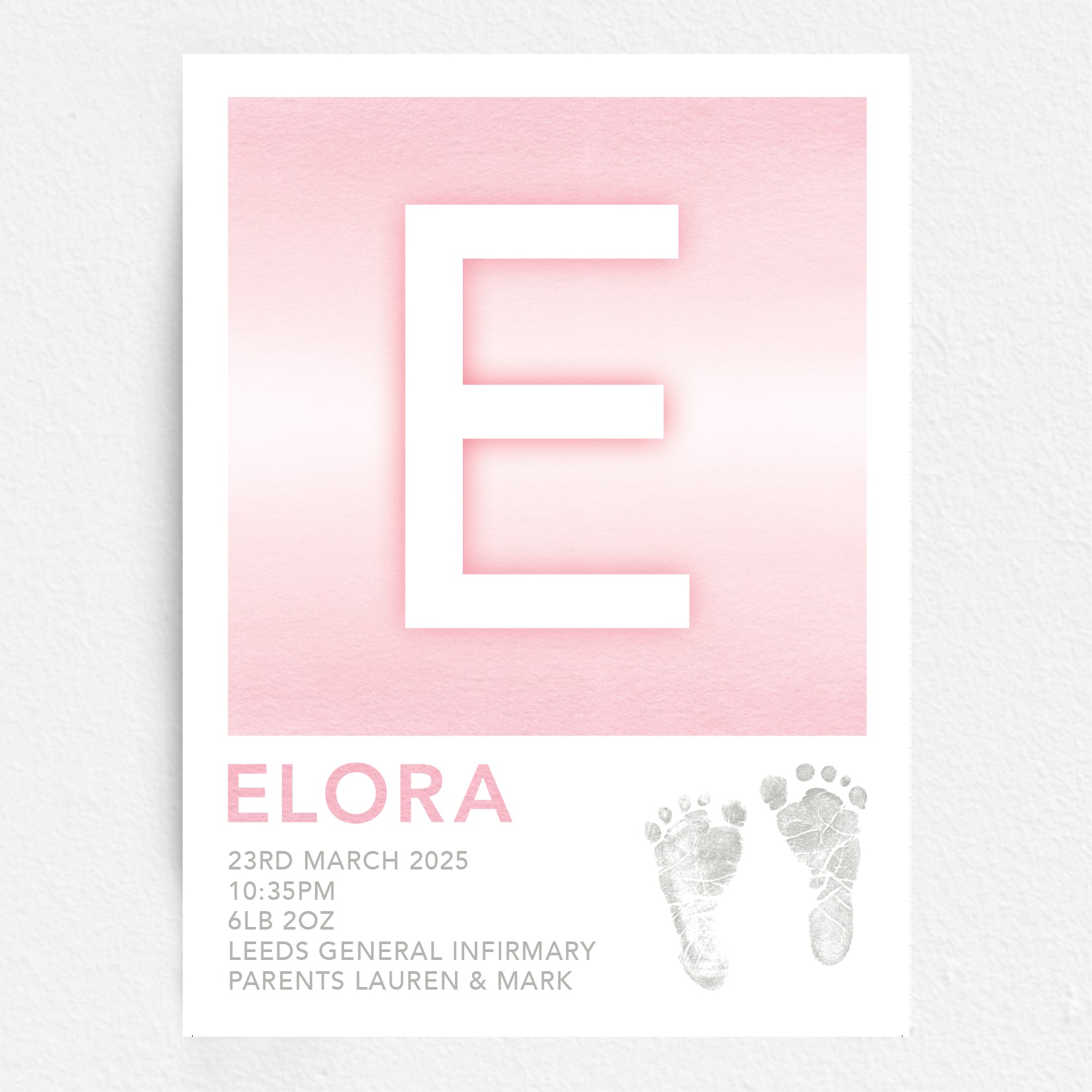 A personalised baby print with the initial 'E' in large pink lettering, birth details, and baby feet prints.
