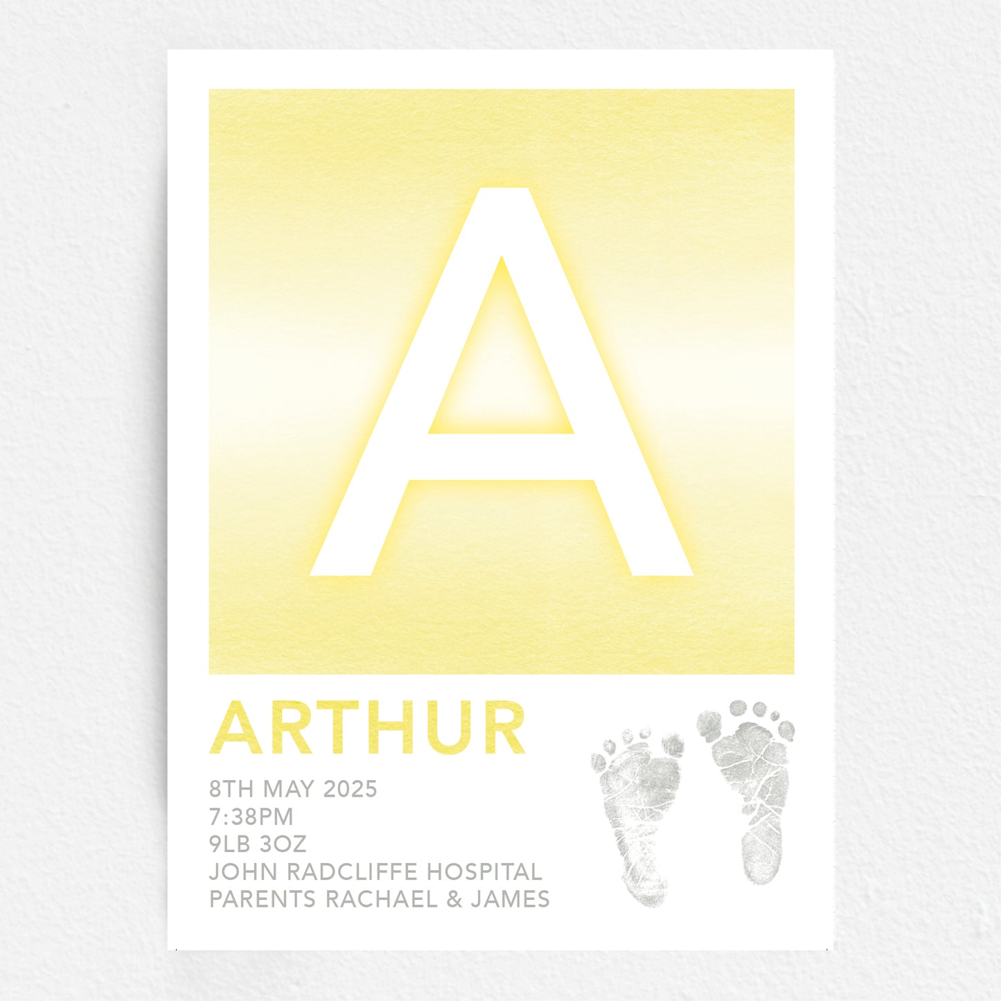 A personalised baby print with the initial 'A' in large yellow lettering, birth details, and baby feet prints.